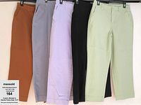 Five pairs of women's stretch denim pants size 10 petite in rust orange, light gray, pastel lavender, black, and light mint green hanging on hangers side by side.