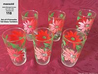 Six tall clear glass tumblers decorated with red and pink poinsettia flowers and green leaves arranged on a red fabric background, showing no chips or cracks.