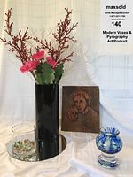 Photo of the full set showing the black glass vase with flowers, the pyrography wooden portrait art behind it, the clear glass vase with marbles on a round mirror base, and the blue glass votive to the right.