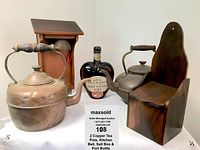 Two vintage copper tea kettles, wooden salt box, call to dinner bell in wooden housing, and heart-shaped port bottle arranged together.