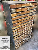 Front view of two vertically stacked metal drawer cabinets with wooden and metal handles. Drawers contain labeled boxes or bags with various hardware items.