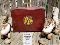 Pair of vintage white ladies roller skates positioned on wooden deck with red vintage BAL-A-ROUE hard case between them, showing logo and handle
