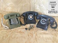 Three vintage telephones with cords and a telegraph Morse code key on a patterned fabric background.