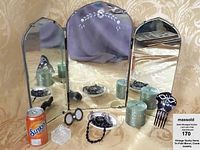 Vintage tri-fold mirror with floral etching on the center panel, displayed open with accompanying items around it including a soda can (not included), porcelain soap dish, jewelry, hair comb, candle, and cut glass bottle.