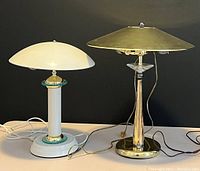 Two vintage table lamps on white surface, black background; brass lamp on right with conical shade, white lamp on left with dome shade.