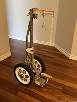 Full view of the antique golf bag holder showing metal frame and attached large wheels on hardwood floor.