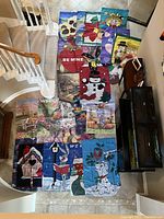 Photo showing all 20 house flags arranged on the floor next to staircase and furniture, showcasing various designs and sizes.