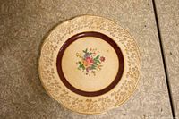 Top view showing plate with floral center, brown band, and gold decorative border with scalloped edges.
