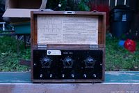 Front view of wooden box with hinged lid open showing the control panel with three dials and instructions inside the lid.