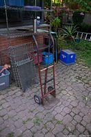 Side angle view of rusted metal hand dolly against brick wall and outdoor shelving