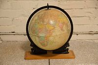 Full globe front showing Africa, Europe and parts of Asia on a wood base with black iron sculptures.