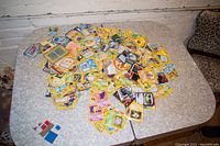 A wide overhead view of a large pile of Pokemon cards spread on a table showing multiple characters and different card backs.
