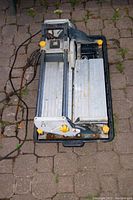 Top-down view of the tile saw showing the sliding aluminum platform, chrome rails, yellow adjustment knobs, and power cord.