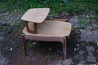 Photo showing two-tier side table stacked on the ground outdoors, highlighting the partially sanded wood surfaces and separated tiers.