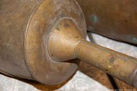 Close-up image showing details of one brass/copper alloy scooper including metal patina and wooden handle attachment.