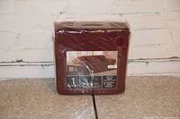 Packaged reddish-brown sofa cover in shrink wrap with label.