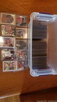 Plastic bin filled with numerous sports cards in hard plastic sleeves and a binder page showing nine cards