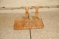 Photo showing the entire set of two pink depression glass candle holders, rectangular tray, and two small round bowls on a stone surface against a brick wall.