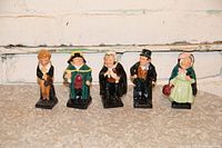 Wide shot of 5 ceramic figurines arranged in a row showing front and base details of each character.