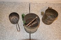 Three vintage metal kitchen sifters placed side by side on a tiled surface showing different sizes and styles.