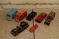Full lot of seven vintage toy cars and one tool accessory displayed together on a textured surface against a brick wall background.