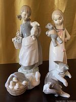 Group photo of four porcelain figurines on dark surface with golden fabric background