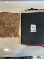 Top-down view showing the antique leather-bound stamp album with visible wear and a black binder next to it containing loose papers.