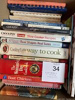 Stack of various cookbooks with visible titles mainly related to chicken, keto diet, slow cooker, and desserts.