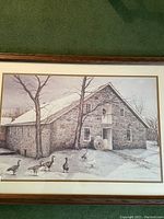 Full view of framed artwork showing a stone building with geese in snow, matted and framed in brown wood frame.