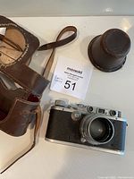 Overview of camera body with attached lens and brown leather carrying case