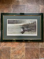 Full view of framed print showing two loons swimming in water with surrounding reeds and trees.