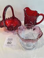 Red glass pitcher, decorative basket, and short bowl displayed together on white surface, showing shape and color.