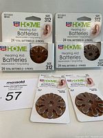 Front view showing two unopened 24-packs and two 8-packs of Rite Aid Home size 312 hearing aid batteries arranged on table with auction lot number included.