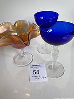 Three glass items on white surface, two cobalt blue stem glasses and one marigold colored compote with ruffled edges.