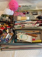 Photo of sewing and crafting supplies including colorful yarn balls, embroidery floss skeins, quilling kit, latch hooks, thread spools, patterns and booklets in two boxes