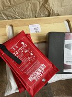 Wooden bed transfer board with hand grips, red JJ Care fire blankets in fabric cases with printed instructions.