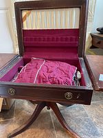 Open wooden vintage drop leaf table showing red fabric lining and drawer with cloth and utensils inside
