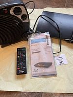 Westpointe fan forced heater and Sony Blu-ray player with remote and manual on light surface.