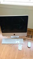 Front view of Apple iMac 20-inch computer with keyboard and mouse on wooden floor