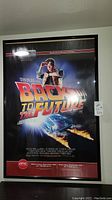 Framed Back to the Future movie poster featuring Marty McFly and hoverboard, black background with prominent title and 25th Anniversary tag.