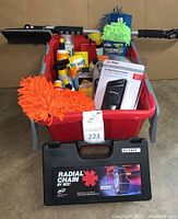 View of all car supplies inside a red plastic bin showing bottles of cleaners, brightly colored microfiber mitts, power inverter box, and a black hard plastic case of tire chains in front.