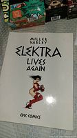 Photo of Elektra Lives Again comic book cover, showing white cover with black text and a stylized drawing of Elektra in red.