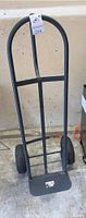 Front view of heavy duty dolly showing black steel frame, two pneumatic tires, rectangular base plate, and curved handle.