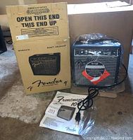 Photo shows Fender Frontman 10G amplifier beside its original cardboard box and owner's manual lying flat on the floor.