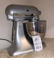 Full side view of the silver KitchenAid stand mixer with stainless steel mixing bowl placed on a countertop, showing overall design and heavy-duty build.