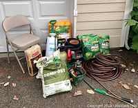 Full lot showing folding chair, wood shavings, compost bag, sprayers, hose nozzles, lawn food bags and coiled hoses