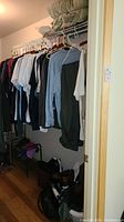 Closet with hanging clothing items including shirts and coats on hangers and shoes on the floor underneath.