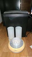 Black Omnitech paper shredder with power cord, beside Bem Ohana Bluetooth speaker and two white cylindrical speakers on a wooden floor