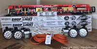 Three boxed Lights of America shop lights, four black LED flashlights, four 6V Rayovac batteries, two coiled 8-foot garage and tool organizer extension cords (white and orange).