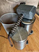Thor's hammer prop placed leaning on two stainless steel pedal bins and one mesh trash bin on wooden floor.